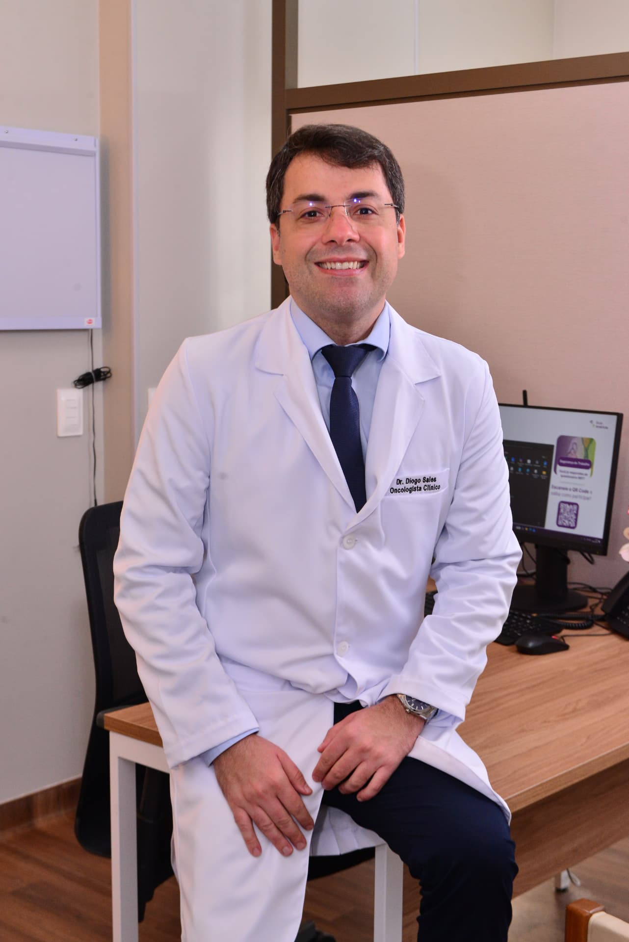 Dr. Diogo Sales sentado no consultório